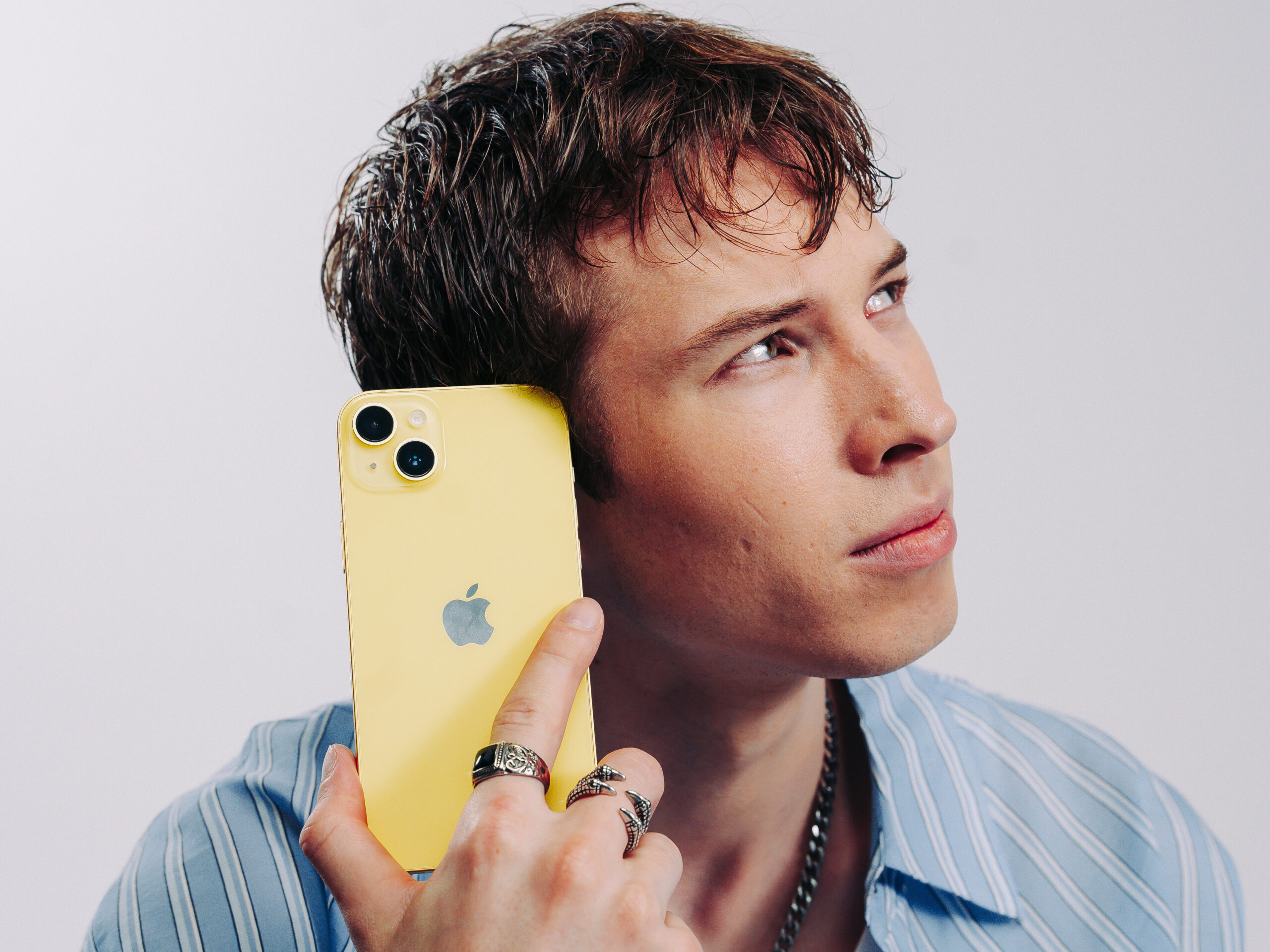 Kille lyssnar efter ljud på iPhone En fundersam kille håller sin iPhone mot örat och försöker lyssna efter ljud